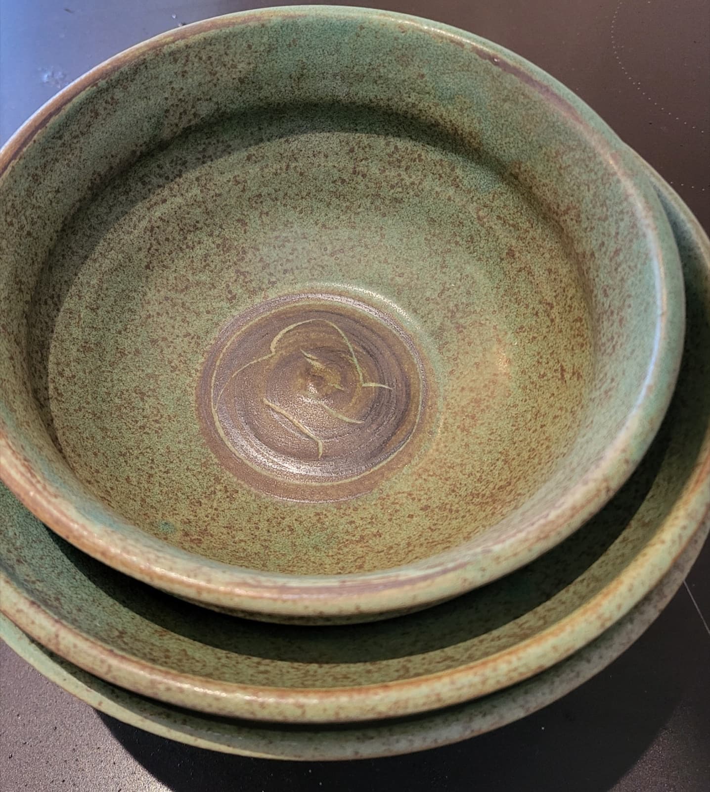 Two stacked stoneware bowls in a soft green glaze with iron-oxide decoration and an impressed medallion in the interior of the inner bowl.