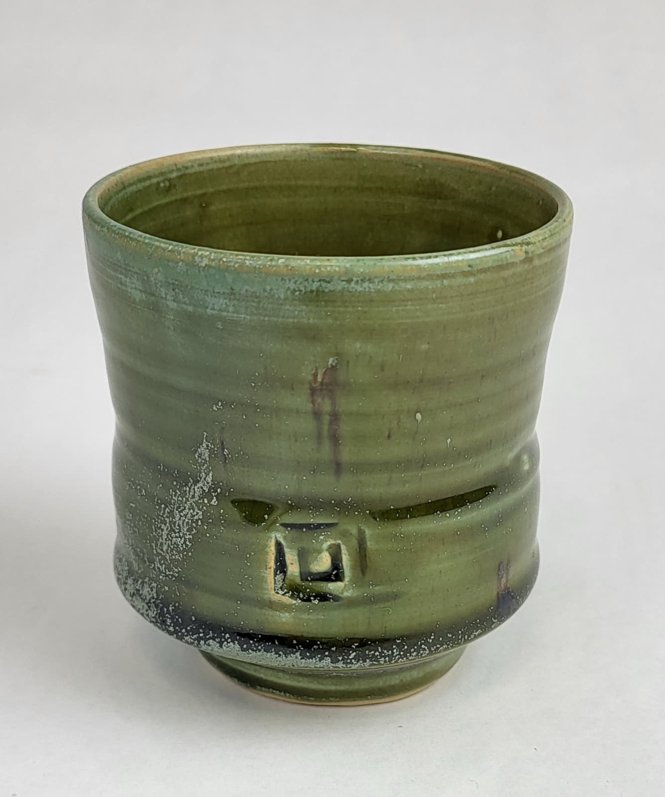 A tall green stoneware tea cup in the yunomi form, with a celadon ash glaze and a small impressed seal near the foot.