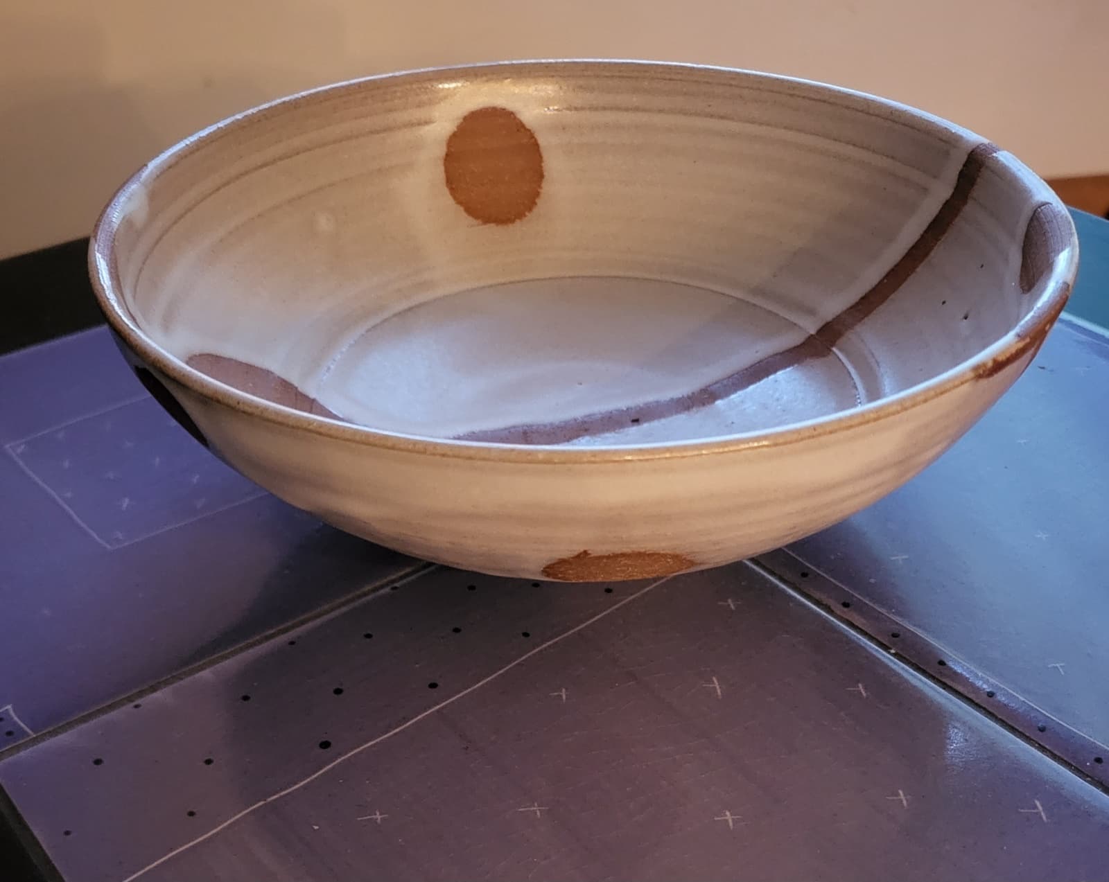 A wide shallow stoneware bowl in a white glaze, with warm rust-colored ovoid spots and a vertical trail left by wax resist.