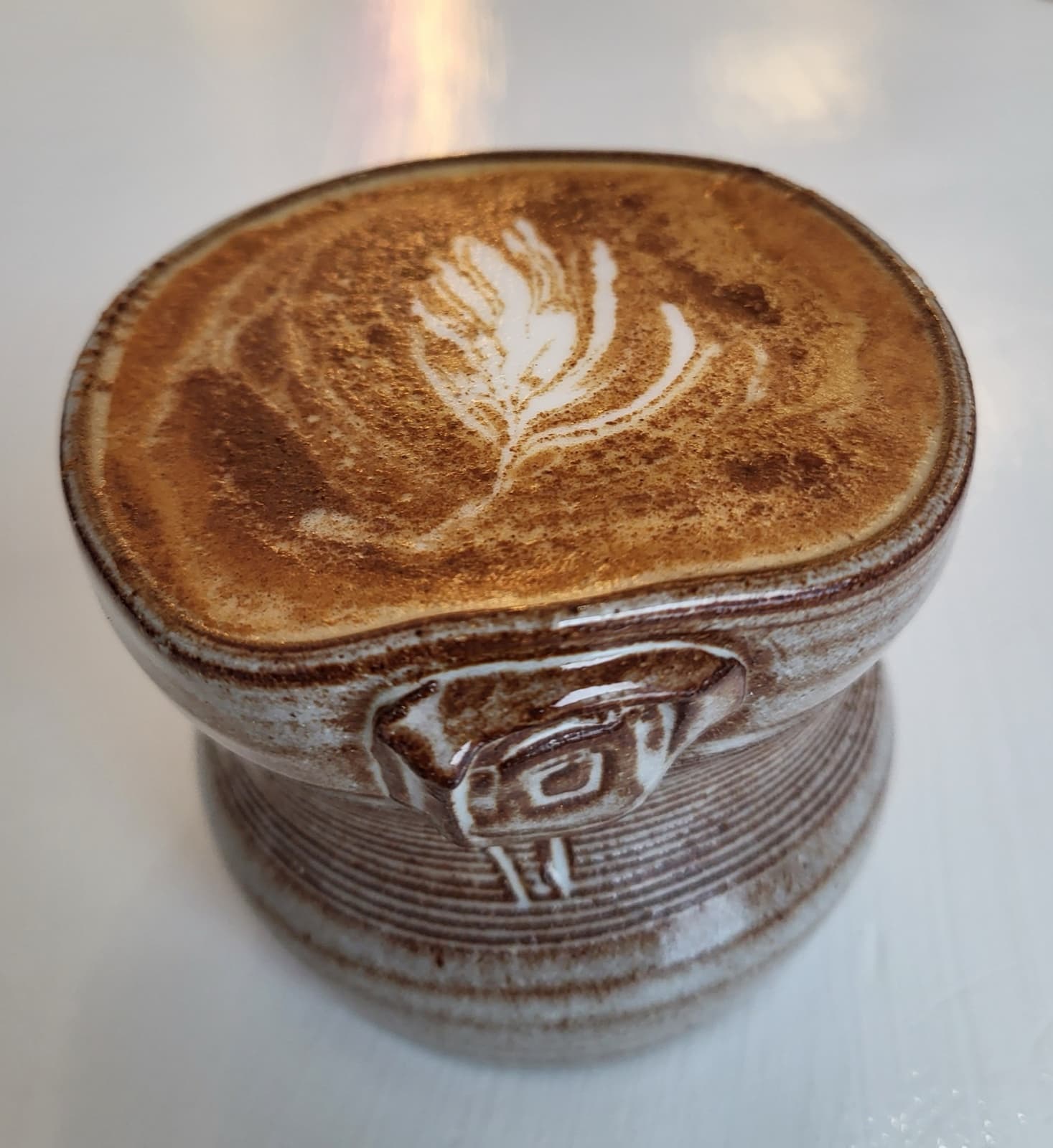 A pinched stoneware bowl with a chop-mark seal, holding a cappuccino with leaf-rosetta latte art.